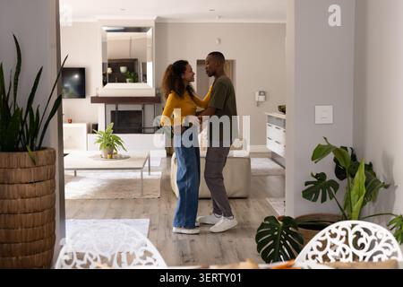 Diverse Paare stehen und halten sich in der Taille im Wohnzimmer mit Sofa, Pflanzen Stockfoto