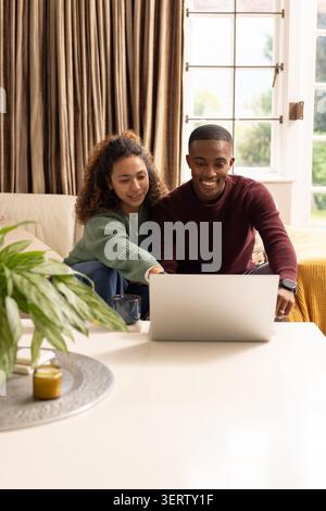 Paare sitzen dicht auf hellem Sofa, mit silbernem Laptop auf weißem Couchtisch mit Becher Stockfoto