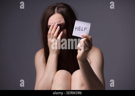 Menschenhandel. Verzweifelte Frau, die Papier hält, mit Worthilfe auf grauem Hintergrund Stockfoto