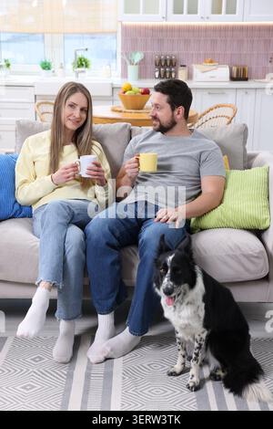 Glückliches Paar trinkt Kaffee und ruht sich mit seinem Hund zu Hause auf dem Sofa aus Stockfoto