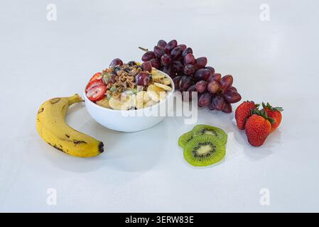 Heller, hochwertiger Shot mit einer Schüssel mit frischem Obst mit Bananen, Trauben, Erdbeeren und Kiwi. Strukturiertes Granola-Oberteil. Farben verbessern die Healt-Funktion Stockfoto