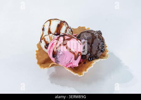 Drei Eislöffel, verschiedene Geschmacksrichtungen, serviert in knusprigem Waffelkegel, garniert mit brauner Schokoladensoße. Studio aufgenommen mit heller Beleuchtung, Promotin Stockfoto