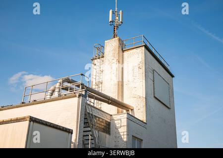 Mobilfunkantenne auf dem Dach eines Industriegebäudes vor blauem Himmel, Mobilfunkturm und Netzwerksenderinfrastruktur Stockfoto