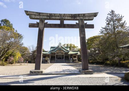 Blick auf das große steinerne Torii-Tor, das zum Hokoku-Schrein führt, umgeben von üppigen Bäumen unter einem klaren blauen Himmel in Osaka, Osaka, Japan. Stockfoto