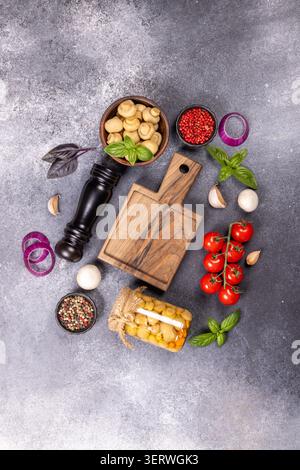 Eingelegte Pilze in einem Glas und einer Schüssel mit frischen Pilzen, Kirschtomaten, Knoblauch, Zwiebeln, Basilikum, und verschiedene Pfefferkörner angeordnet Stockfoto