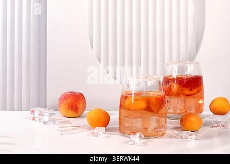 Eis-Pfirsichtee oder Cocktail mit Eiswürfeln und Aprikosen, Rezept für ein erfrischendes Sommergetränk. Zwei Gläser mit Pfirsichfrucht-Limonade auf einem eleganten Tisch, Stockfoto
