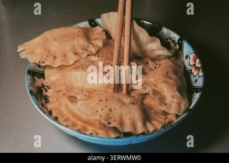 Eine Schüssel mit goldenen Klößchen, bekannt als Dim Sum, mit schwarzem Pfeffer bestreut, steht bereit zum Genießen. Ein Paar Holzstäbchen liegt oben auf. Stockfoto
