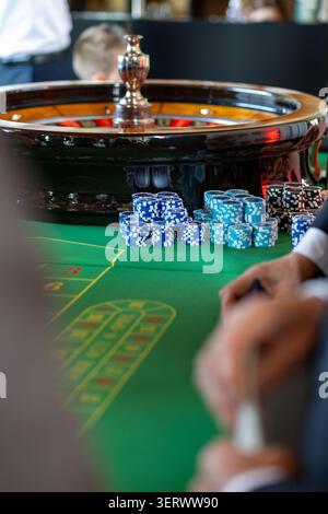 Gruppen von Menschen versammeln sich um einen grünen Roulette-Tisch in einem Kasino. Chips sind stapelweise angeordnet. Die Spieler konzentrieren sich auf das Spiel. Die Einstellung ist Stockfoto