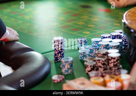 Die Spieler konzentrieren sich auf ein Spiel an einem Casino-Tisch mit bunten Chips, die ordentlich gestapelt sind. Die Atmosphäre ist lebhaft, wenn die Teilnehmer ihre Wetten abschließen. Stockfoto