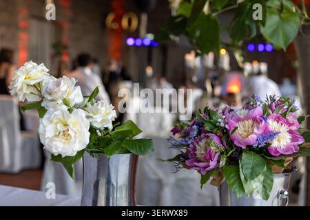 Blumenarrangements werden auf Tischen in einem Veranstaltungsort platziert. Die Gäste sitzen und unterhalten sich. Die Atmosphäre ist lebhaft mit Dekorationen und Licht Stockfoto