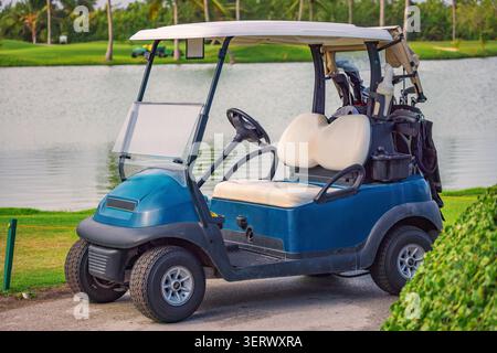 Blauer Golfwagen mit Clubs, die in der Nähe eines Sees im Punta Cana Resort geparkt sind Stockfoto