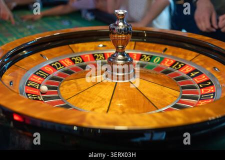 Eine Gruppe von Leuten versammelt sich um den Roulette-Tisch. Sie legen abwechselnd Wetten ab, während sich der Croupier darauf vorbereitet, das Rad zu drehen. Die Atmosphäre ist lebhaft Stockfoto