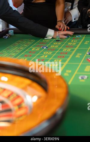 Eine Gruppe von Leuten versammelt sich an einem Roulette-Tisch bei einem Casino-Abend-Event. Sie platzieren Wetten, während sie miteinander interagieren. Die Atmosphäre ist lebhaft Stockfoto