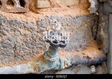 Alter Wasserhahn mit einer beschädigten Wand im Hintergrund Stockfoto