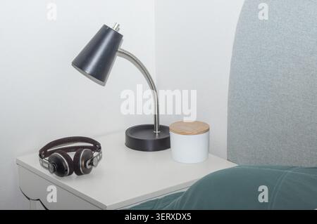 Es gibt eine Schreibtischlampe und Kopfhörer auf dem Nachttisch. Stockfoto