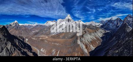 Blick aus der Vogelperspektive auf den Gipfel des Ama Dablam, der über dem zerklüfteten, schneebedeckten Himalaya-Gebirge mit tiefen Tälern und einem klaren blauen Himmel in Nepal aufsteigt. Stockfoto