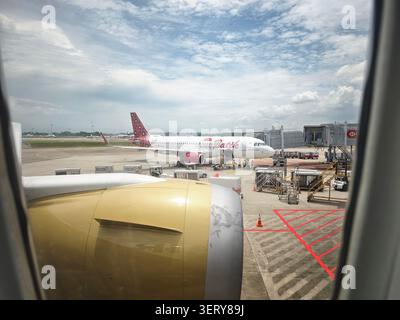 Singapur - 30. September 2025: Ein Flugzeug parkt am Gate, während ein anderes Flugzeug sich während des Tages auf der Start- und Landebahn eines stark frequentierten Flughafens vorbereitet. Stockfoto