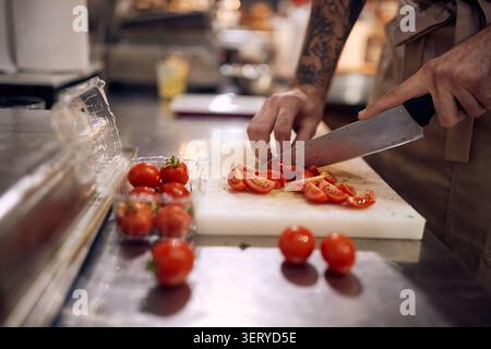 Kochen Sie in professioneller, moderner Küche, Restaurant-Konzept. Nahaufnahme der Köche, die Tomaten mit einem Messer hacken. Stockfoto