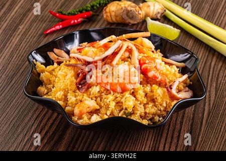 Lebendige Schüssel mit frittiertem Reis und saftigen Garnelen, zartem Tintenfisch. Kräftiger gelber Reis, hellrote Chilis, grüne Limette, aromatisches Zitronengras Stockfoto