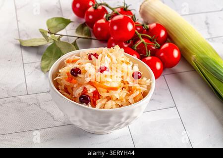 Weiße Schüssel mit traditionellem Sauerkraut mit Preiselbeeren geriebenen Karotten. Frische Kirschtomaten auf Reben, grüner Lauch, Lorbeerblätter sind auf hellem M angeordnet Stockfoto