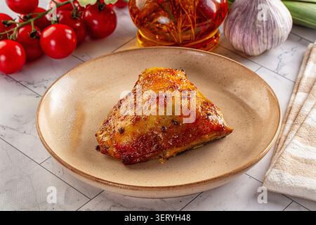 Goldener gerösteter Hähnchenschenkel auf rustikalem Teller umgeben von frischen roten Tomaten, Knoblauch und Olivenöl. Lebensmittelfotografie mit großem Winkel und natürlichem Licht. H Stockfoto