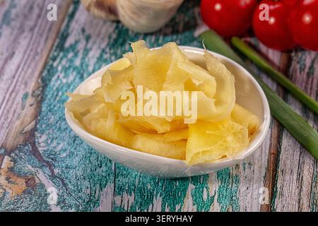 Nahaufnahme getrockneter Ananasscheiben in einer weißen Schüssel, auf eine rustikale Holzoberfläche gelegt. Frische rote Tomaten und grüne Zwiebeln im Hintergrund. Helles l Stockfoto