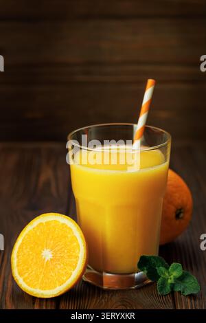 Glas frisch gepresster Orangensaft mit gestreiftem Strohhalm, Minze und Zitrusfrüchten auf rustikalem Holzuntergrund Stockfoto