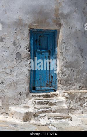 Alte blaue Holztür mit abblätternder Farbe in der weißen Wand mit Stufen Stockfoto