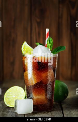Cuba libre Cocktail mit Rum, Cola, frischer Limette und Minze im Glas mit Eis auf Holzuntergrund Stockfoto