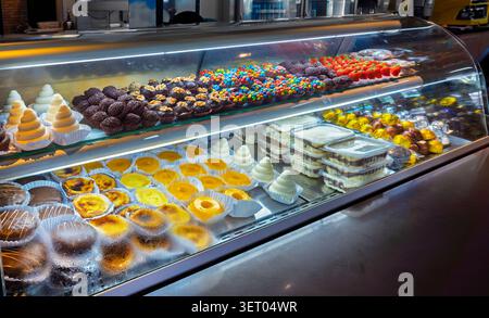 Eine Glasvitrine in einem Süßwarengeschäft gefüllt mit verschiedenen brasilianischen Süßigkeiten wie Brigadeiros, Chinden, Pastell de Nata, Honigkuchen (pão de mel) Stockfoto