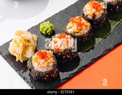 Knusprige, frittierte Tempura-Sushi-Brötchen werden auf Steinteller serviert. Warme gebackene Brötchen sind mit Tartar aus gewürfelten Meeresfrüchten und hellem Tobiko-Kaviar dekoriert. Stockfoto