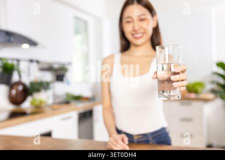 Lächelnde junge Frau, die ein Glas reinem Wasser in der Küche anbietet Stockfoto