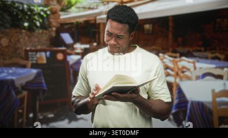 Ein Mann, der ein offenes Buch liest und eine Seite mit einer erhöhten Augenbraue in einem Straßencafé umringt von Tischen und Stühlen dreht; Neugier reflektiert. Stockfoto