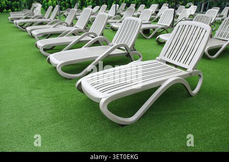 Reihen leerer Plastikliegen auf einem grünen Rasen. Konzept für Erholungsangebote im Sommer, Gastgewerbe und Ferienimmobilienstrategie. Stockfoto