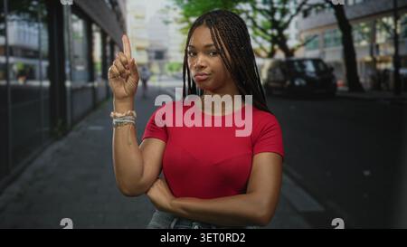 Frau zeigt mit überkreuzten Armen und sichtbaren Armbändern den Zeigefinger auf die Straße; Selbstbewusstsein. Stockfoto