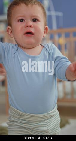 Der Junge weint und greift nach einem Spielzeug, während sich die Pflegekraft in einem Gebäude mit einem Taschentuch das Gesicht abwischt. Stockfoto
