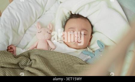 Baby schlaft in der Wiege mit sichtbarer linker Hand und zwei gestrickten Häschen-Spielzeugen auf einer weichen Decke im Kinderzimmer; ruhiger Komfort. Stockfoto