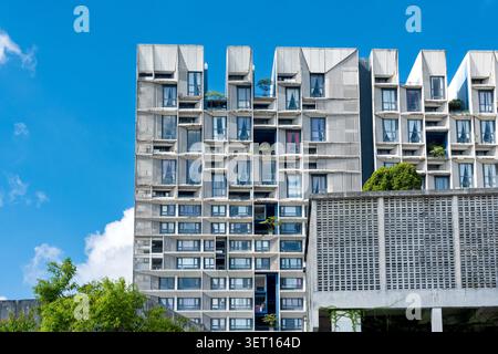Ein modernes mehrstöckiges Wohngebäude mit einer komplexen Betonfassade, geometrischen Fenstern und grünen Balkonpflanzen vor einem hellen Stockfoto
