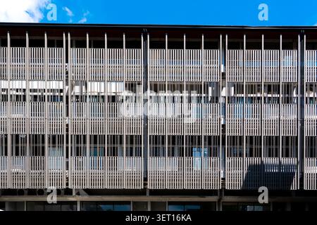 Ein geradeaus architektonisches Bild, das eine zeitgenössische Gebäudefassade zeigt, die mit einem sich wiederholenden Muster aus grauen vertikalen Sonnenläden oder Lamellen bedeckt ist (Fortsetzung) Stockfoto
