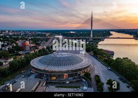 Drohnenansicht der Ada-Brücke und des Belgrader Messekomplexes entlang der Save in Belgrad, Serbien, während Sonnenuntergang. Das Foto nimmt zwei auf Stockfoto