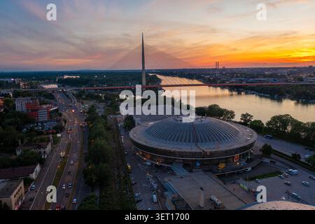 Drohnenansicht der Ada-Brücke und des Belgrader Messekomplexes entlang der Save in Belgrad, Serbien, während Sonnenuntergang. Das Foto nimmt zwei auf Stockfoto