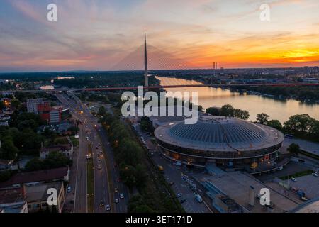 Drohnenansicht der Ada-Brücke und des Belgrader Messekomplexes entlang der Save in Belgrad, Serbien, während Sonnenuntergang. Das Foto nimmt zwei auf Stockfoto