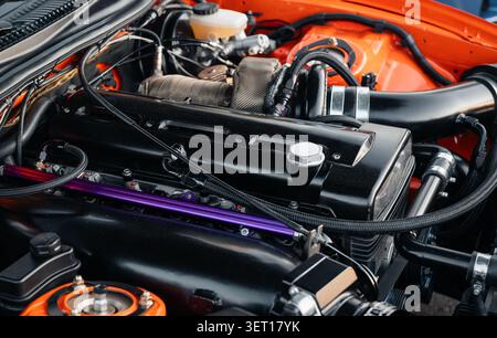 Motorraum ein oranger Sportwagen aus den 1990er Jahren mit Reihensechszylindermotor. Nahaufnahme eines modifizierten Motors mit schwarzem Zylinderkopf und Einlassleitung. Stockfoto