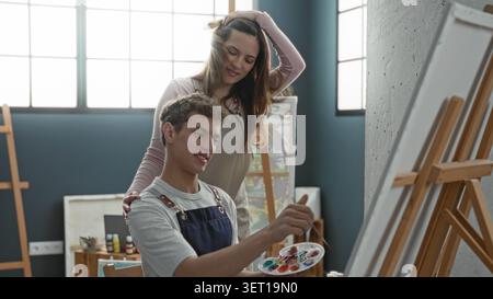 Mann malte auf Leinwand mit Palette und Pinsel, Frau Hand auf der Schulter im Atelier; Mentorenruhe. Stockfoto