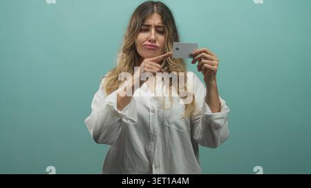 Die Frau zeigt mit dem Finger auf die Kreditkarte, während sie die Karte an der Wand des blaugrünen Studios hält; Frustration Misstrauen. Stockfoto