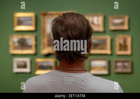 Museumsbesucher stehen vor einer Gemäldesammlung und studieren die Ausstellung sorgfältig. Stockfoto