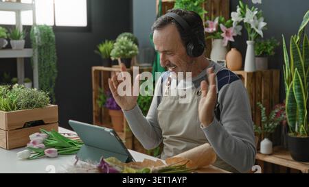 Mann mit Kopfhörern lächelt, Hand auf Tablet, das Tulpen im Blumenladen des Studios arrangiert; Bastelzufriedenheit. Stockfoto