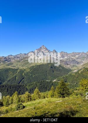 Malerischer Panoramablick auf den Monviso, den höchsten Gipfel der Kottischen Alpen, der sich über dem alpinen Dorf Crissolo und den üppigen grünen Kiefernwäldern erhebt. Vie Stockfoto