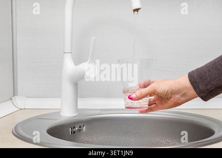 Eine Frau füllt ein Glas mit sauberem gefiltertem Leitungswasser zum Trinken in der Küche. Stockfoto