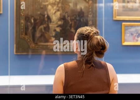 Eine Person steht vor einem großen Gemälde in einem Kunstmuseum. Der Besucher konzentriert sich auf das Kunstwerk. Die Ausstellung ist gut beleuchtet und hat mehrere Rahmen Stockfoto